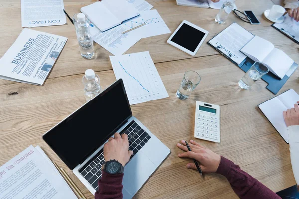 Vista recortada de empresarios sentados en el escritorio cerca de dispositivos digitales, documentos y vasos con agua - foto de stock