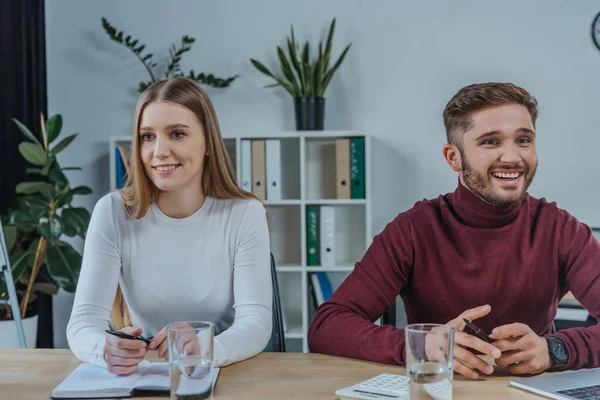 Young, smiling businessman and businesswoman sitting at desk in meeting room — Stock Photo