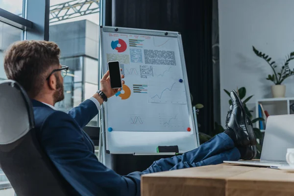 Young businessman sitting with legs on table and taking selfie on smartphone — Stock Photo