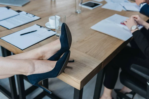 Vista recortada de la mujer de negocios en zapatos de tacón alto sentado con las piernas en el escritorio - foto de stock