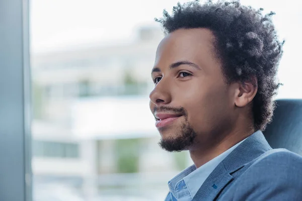 Jeune homme d'affaires afro-américain souriant près de la fenêtre dans le bureau — Photo de stock