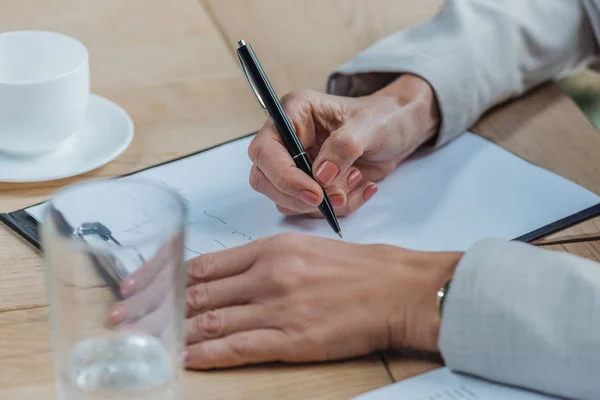 Ausgeschnittene Ansicht einer Geschäftsfrau, die mit Stift auf Klemmbrett schreibt — Stockfoto