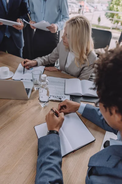 Mature businesswoman pointing with pen at document during business meeting with young multicultural colleagues — Stock Photo