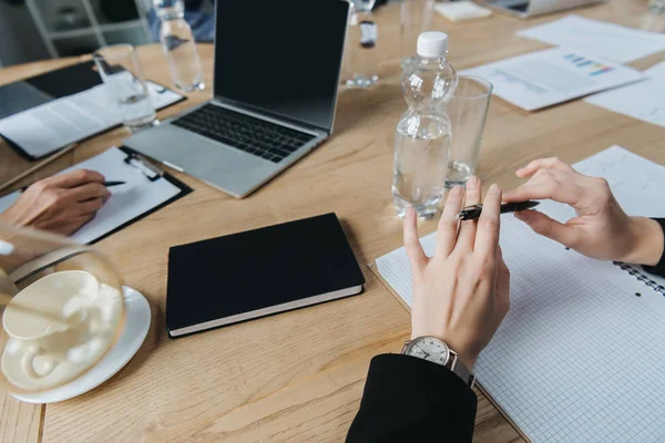 Cropped view of businesswomen at desk with laptop, notebooks, bootles with water and documents in meeting room — Stock Photo