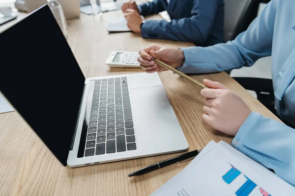 Vista recortada del hombre de negocios sosteniendo lápiz mientras está sentado cerca de la computadora portátil en la sala de reuniones - foto de stock