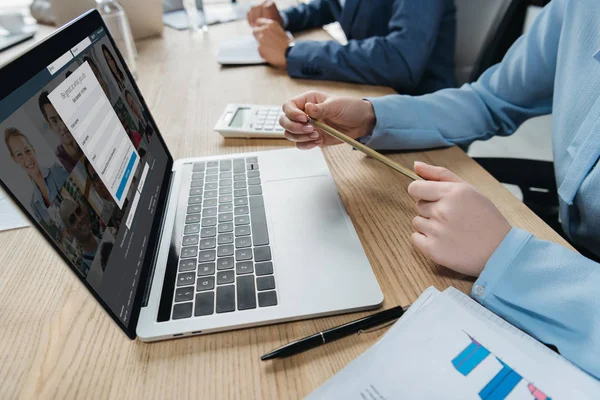 KYIV, UCRANIA - 1 de octubre de 2019: Vista recortada del hombre de negocios sentado en la sala de reuniones cerca de la computadora portátil con el sitio web Linkedin en la pantalla . - foto de stock