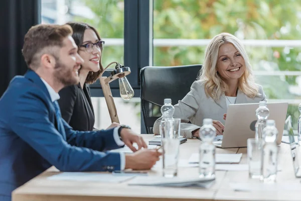 Fröhliche Geschäftsleute, die mit Dokumenten und Wasserflaschen im Besprechungsraum neben dem Schreibtisch sitzen — Stockfoto