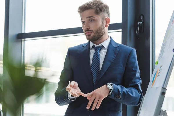 Selective businessman counting by fingers while standing near flipchart at business meeting — Stock Photo
