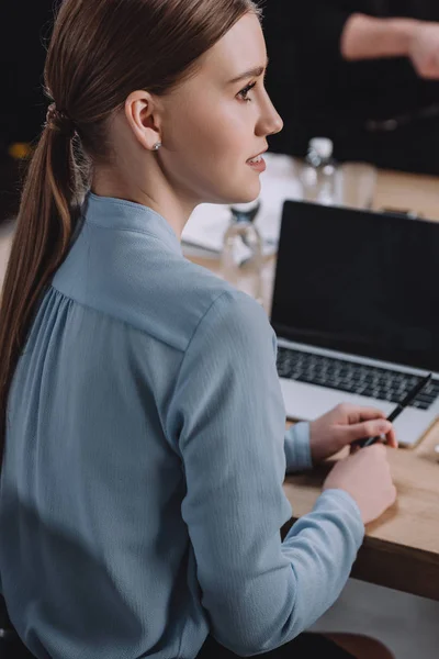 Young, attentive businesswoman sitting in meeting room near laptop with blank screen — Stock Photo