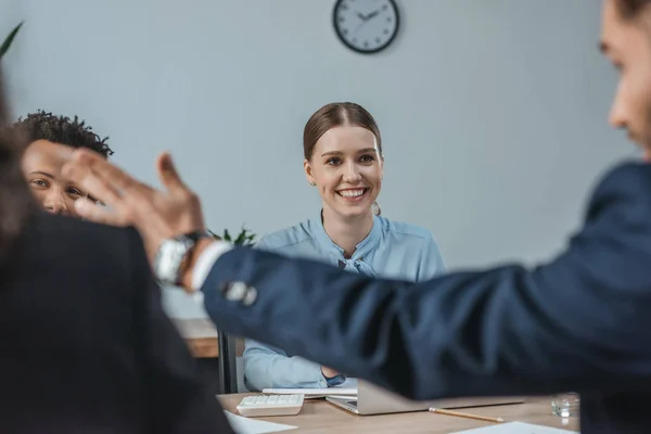 Selective focus of smiling businesswoman looking at colleague pointing with hand near multicultural coworkers — Stock Photo