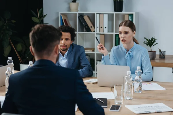 Joven empresaria hablando con colegas multiculturales durante la reunión de negocios - foto de stock