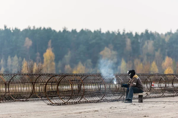 LVIV, UCRANIA - 23 DE OCTUBRE DE 2019: soldador en máscara protectora y soldadura uniforme construcción metálica - foto de stock