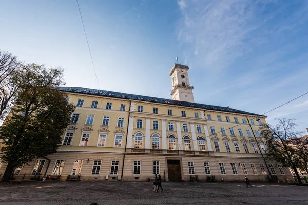 LVIV, UKRAINE - OCTOBER 23, 2019: facade of lviv city hall tower and people walking along street — Stock Photo