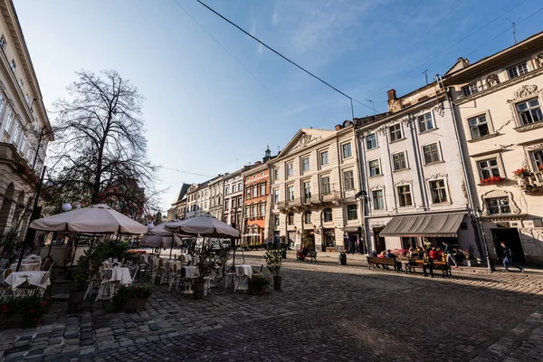 LVIV, UCRANIA - 23 de octubre de 2019: personas sentadas en la cafetería de la calle cerca de casas antiguas en el centro de la ciudad — Stock Photo