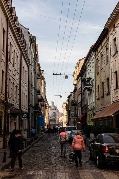 LVIV, UKRAINE - OCTOBER 23, 2019: parked cars and people walking near house with cyrillic lettering on signboard — Stock Photo