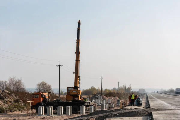 LVIV, UKRAINE - 23 OCTOBRE 2019 : camion avec grue avec lettrage en teck et blocs de béton près des travailleurs sur l'autoroute — Photo de stock