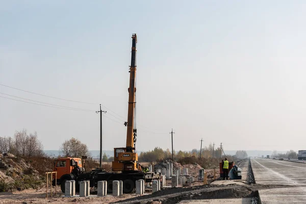 LVIV, UCRANIA - 23 DE OCTUBRE DE 2019: camión con grúa con letras de roble, y bloques de hormigón cerca de los trabajadores en la carretera - foto de stock