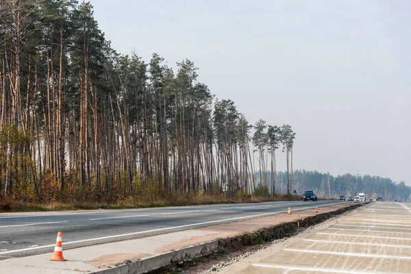 LVIV, UKRAINE - OCTOBER 23, 2019: roadwork cones near highway with car moving with lighting headlamps in ukraine — Stock Photo