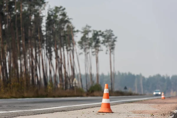 Conos de carretera cerca de la carretera con el coche en movimiento con faros de iluminación en Ucrania - foto de stock