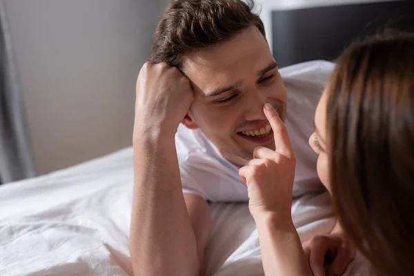 Selective focus of cheerful girl touching nose of happy boyfriend in bedroom — Stock Photo