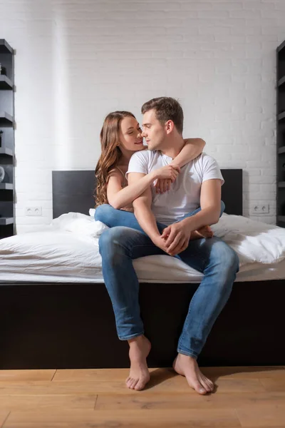 Menina feliz abraçando bonito namorado sentado na cama — Fotografia de Stock