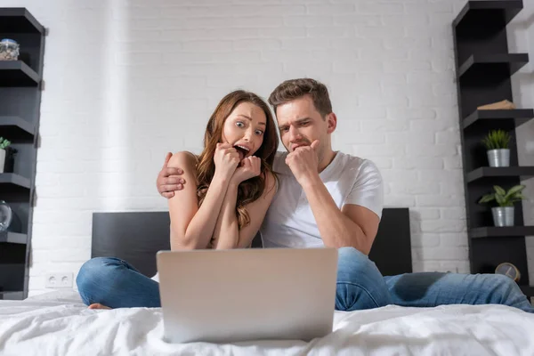 Emotional couple watching scary movie on laptop in bedroom — Stock Photo