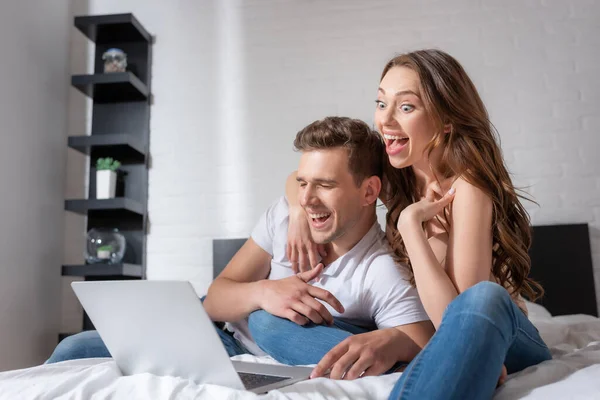 Cheerful woman and man laughing while watching comedy movie on laptop in bedroom — Stock Photo