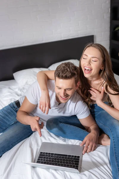 Glücklicher Mann, der mit dem Finger auf Laptop zeigt, während er lacht und Film mit Freundin schaut — Stockfoto