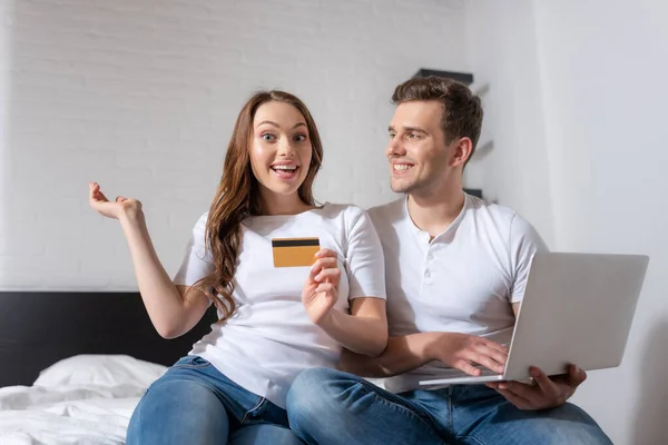 Happy woman holding credit card near cheerful man and laptop — Stock Photo