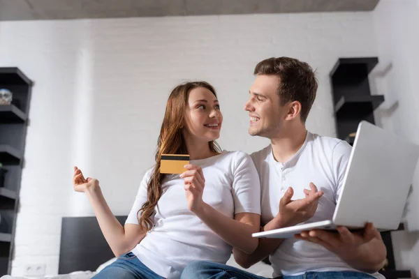 Happy girl holding credit card and man using laptop while looking at each other — Stock Photo