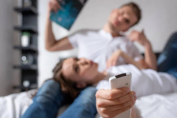 Selektiver Fokus der Frau mit Fernbedienung von einer Klimaanlage, die in der Nähe eines Mannes liegt, der ein Magazin hält, während er sich heiß fühlt — Stockfoto