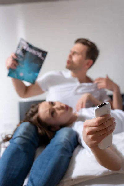 Selective focus of girl with remote controller from air conditioner lying near man holding magazine while feeling hot — Stock Photo