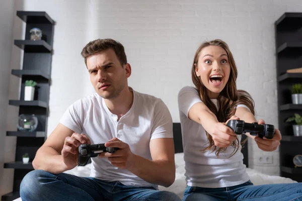KYIV, UKRAINE - MAY 15, 2020: excited woman and displeased man playing video game in bedroom — Stock Photo