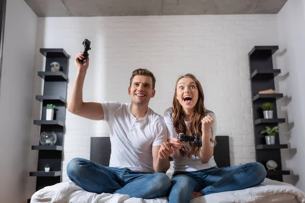 KYIV, UKRAINE - MAY 15, 2020: excited woman and happy man playing video game in bedroom — Stock Photo