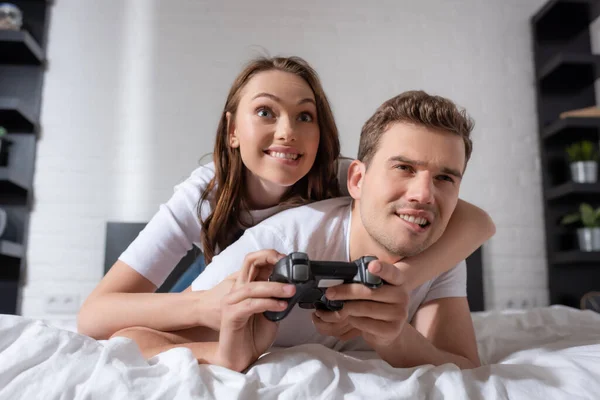 КИЕВ, УКРАИНА - 15 мая 2020 года: веселая женщина и мужчина играют в видеоигры в спальне — стоковое фото