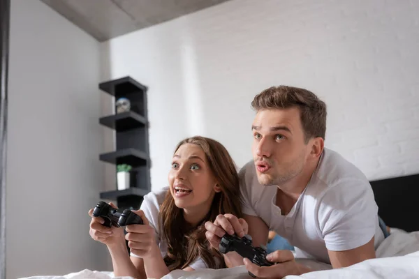 KYIV, UKRAINE - MAY 15, 2020: excited woman and emotional man playing video game in bedroom — Stock Photo