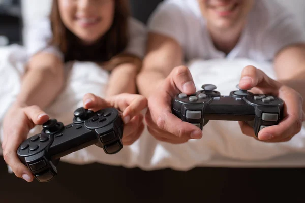 KYIV, UCRANIA - 15 de mayo de 2020: enfoque selectivo de la mujer y el hombre feliz sosteniendo joysticks y jugando videojuegos en el dormitorio - foto de stock