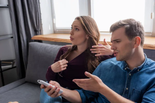 Fille assise sur le canapé près de l'homme pointant avec la main à la télécommande du climatiseur tout en se sentant chaud — Photo de stock