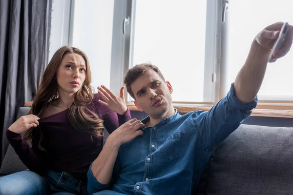 Girl sitting on sofa near displeased boyfriend holding remote controller from air conditioner while feeling hot — Stock Photo