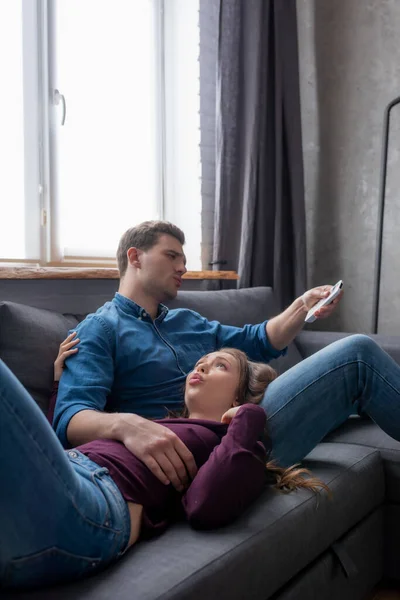 Femme mécontente couché près petit ami tenant télécommande de climatiseur tout en se sentant chaud — Photo de stock