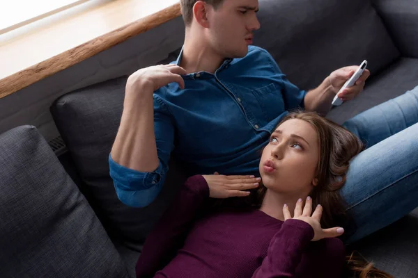 Woman with duck face lying near boyfriend holding remote controller from air conditioner while feeling hot — Stock Photo