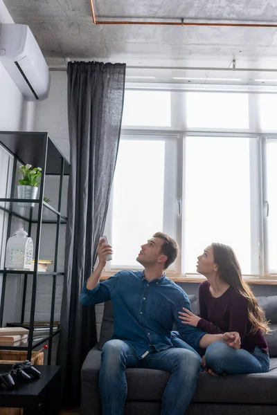 Mann und Frau blicken auf Klimaanlage, während sie auf dem Sofa sitzen — Stockfoto