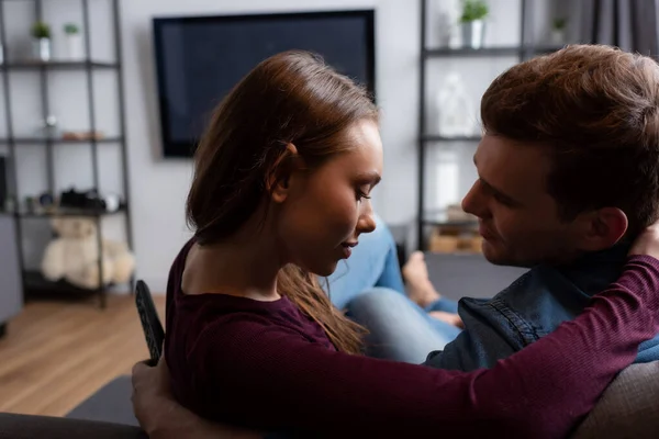 Hombre sosteniendo mando a distancia cerca atractiva novia en sala de estar - foto de stock