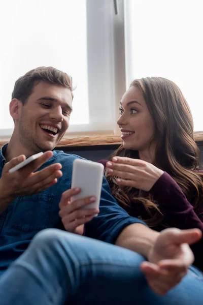 Selektiver Fokus des glücklichen Mannes, der in der Nähe seiner Freundin auf das Smartphone schaut — Stockfoto