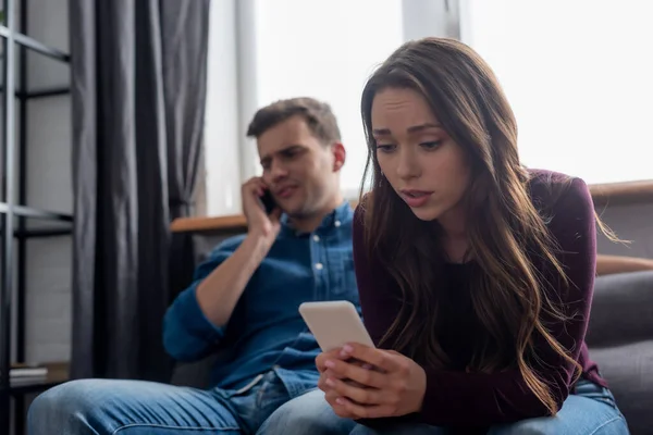 Foco seletivo de mensagens de texto menina enquanto segurando smartphone e homem falando na sala de estar — Fotografia de Stock