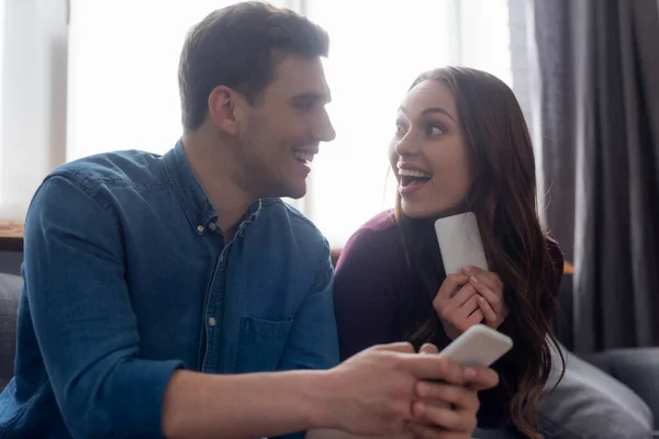 Вибірковий фокус веселої пари, дивлячись один на одного і тримаючи смартфони — стокове фото