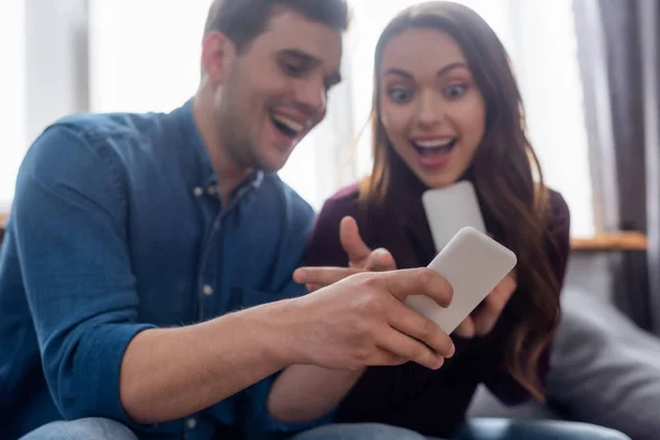 Selective focus of cheerful man pointing with finger at smartphone near excited girl — Stock Photo