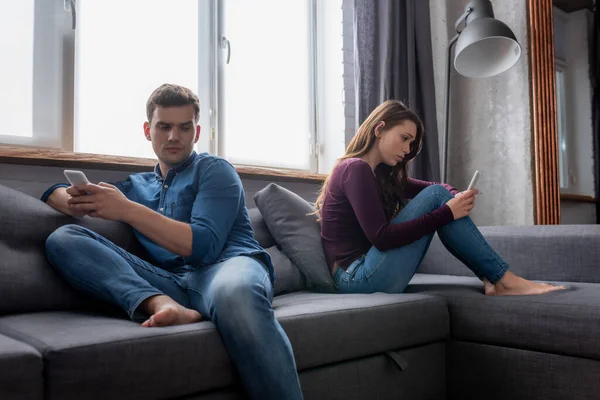 Homem e mulher sentados no sofá e usando smartphones — Fotografia de Stock