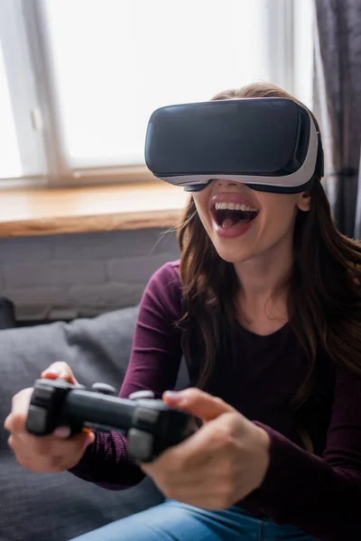 KYIV, UCRANIA - 15 de mayo de 2020: enfoque selectivo de la mujer emocionada en los auriculares de realidad virtual que sostiene el joystick mientras juega a videojuegos - foto de stock