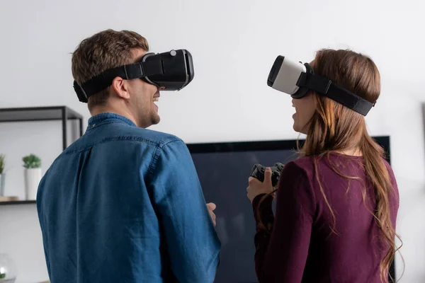 KYIV, UCRANIA - 15 de mayo de 2020: pareja alegre en auriculares de realidad virtual jugando videojuegos en la sala de estar - foto de stock
